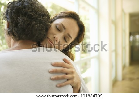 Portrait of a mature couple hugging by large glass doors at home.