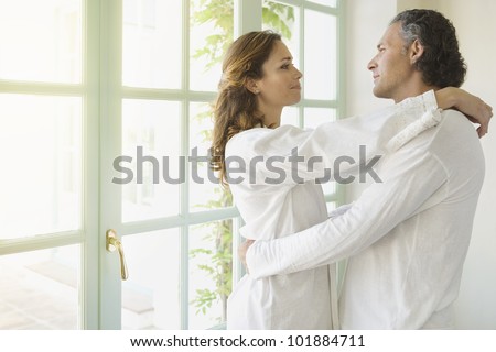 Portrait of a mature couple hugging at home, standing by large garden doors.