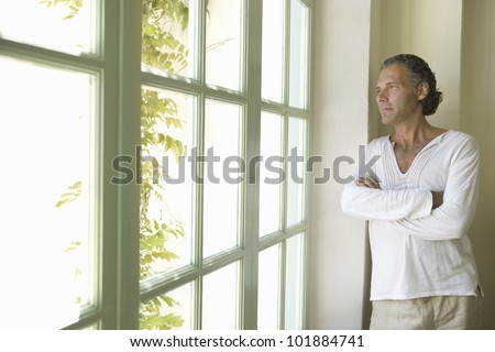 Professional mature man at home looking out a large window into a sunny day.