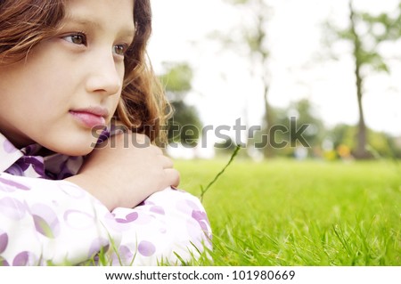 Close up portrait of a young girl laying down on green grass in the park, looking ahead.