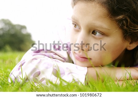 Close up portrait of a young girl laying down on green grass in the park, looking ahead.