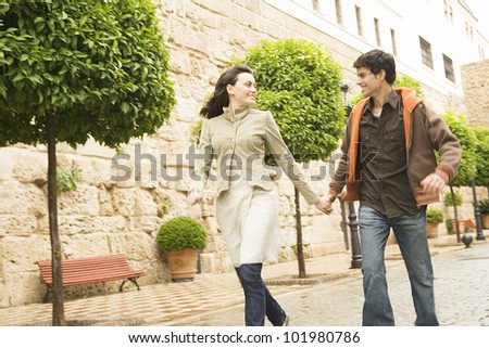 Young tourist couple holding hands and running through a town\'s square.