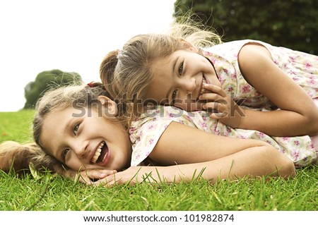 Two sisters laughing and playing in the park, laying down.