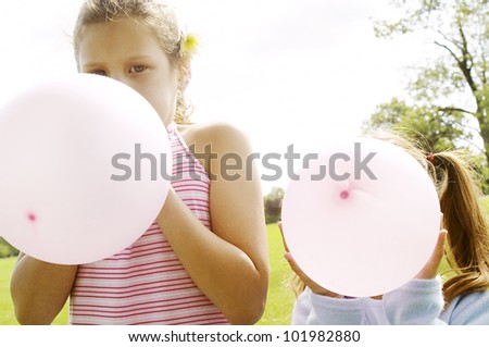Two girl blowing up pink balloons with their face hiding behind the balloons.