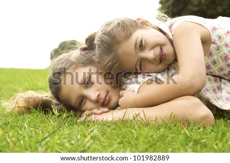 Two sisters laying down on top of each other and smiling in the park.