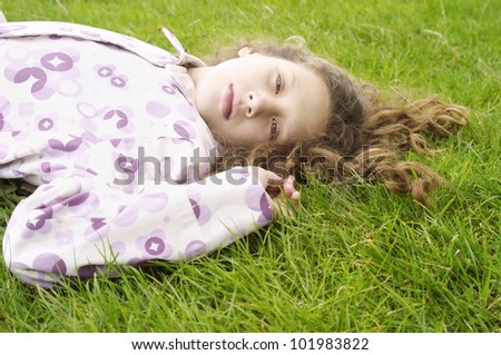 Portrait of a girl laying down on green grass and wearing a coat.