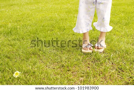 Young girl\'s feet wearing summer sandals and standing on bright green grass in the park.