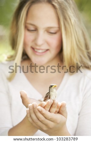 Close up portrait of a girl in the garden, holding a bird in her hands and smiling.