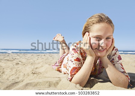 Girl laying down on a golden sand beach, smiling at the camera and wearing a floral dress.