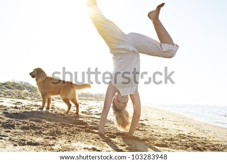 Girl with dog on the beach, doing cartwheels with the sun filtering through.