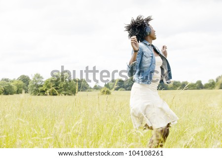 Young black woman dancing in a long grass field while listening to music with her headphones.
