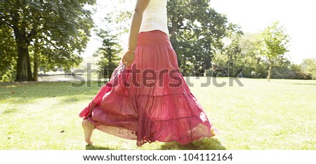 Woman\'s body section walking across a park, wearing a bright pink skirt in the warm light.