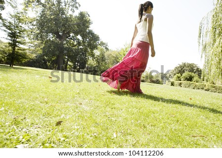 Young woman walking across a park, wearing a bright pink skirt in the warm light.