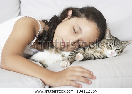 Young girl and kitten sleeping on a white sofa at home.