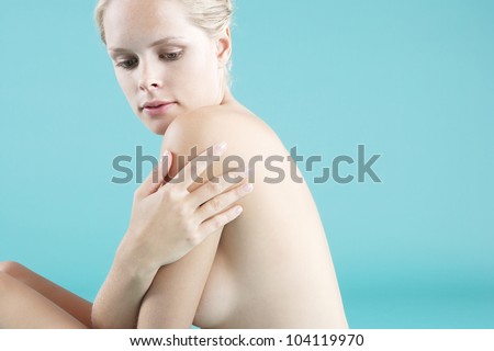 Portrait of a young attractive woman sitting down naked on a blue background.