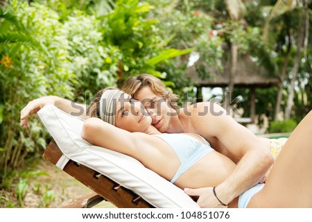 Young couple hugging on a sun bed in a villa\'s tropical garden while on vacation.