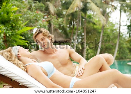 Young couple relaxing on a sun bed in a villa\'s tropical garden while on vacation.