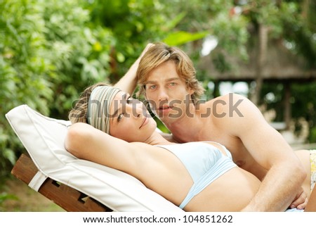 Young couple relaxing on a sun bed in a villa\'s tropical garden while on vacation.