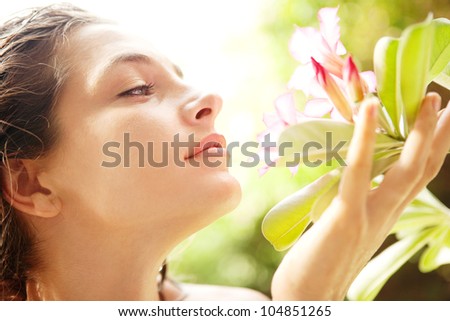 Close up profile view of a young attractive girl smelling a tropical pink flower in an exotic garden.