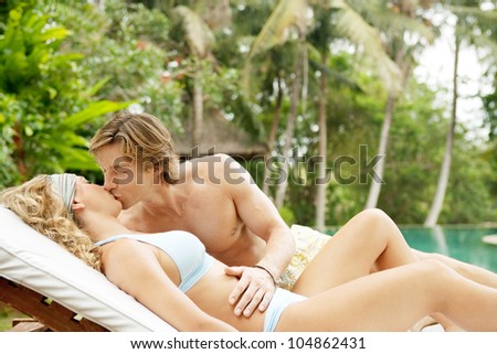 Young couple relaxing on a sun bed and kissing in a villa\'s tropical garden while on vacation.