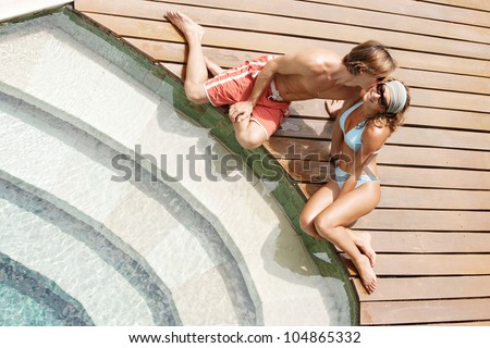 Over head view of an attractive couple kissing while they relax by a swimming pool\'s steps in a hotel garden.