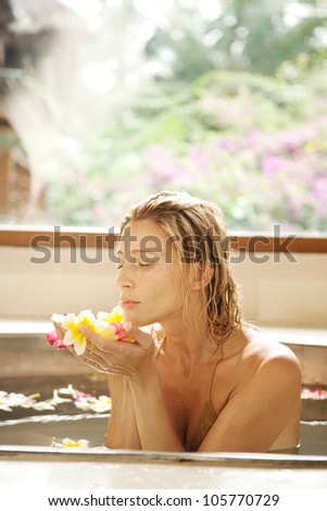 Young woman smelling flowers in her hands while in a flower bath tub in a health spa.