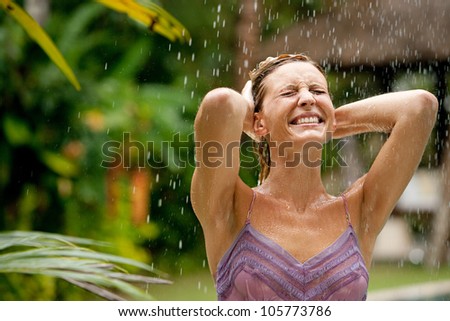 Portrait of a beautiful happy woman enjoying tropical rain falling on her in an exotic garden.