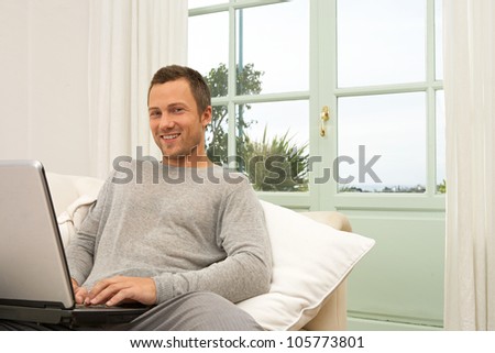 Young professional man using a laptop computer while sitting on a white sofa at home.