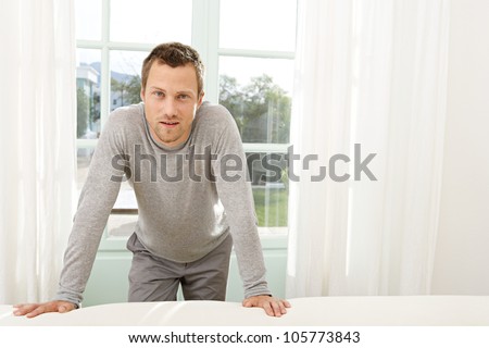Professional young man leaning on the back of a white sofa at home while standing by large garden doors.