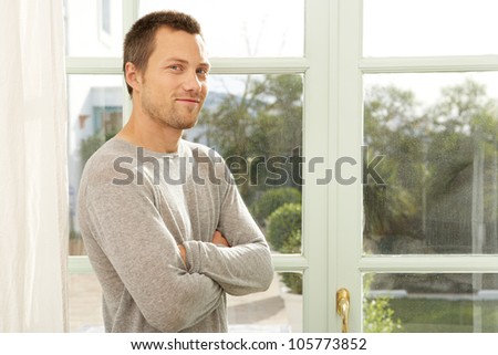 Young professional man standing by garden doors at home, smiling.