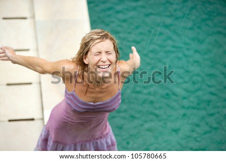 Over head view of a woman by a swimming pool under falling rain in the summer, smiling.
