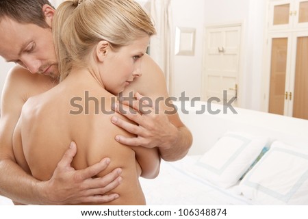 Young man hugging a nude woman in a bedroom.