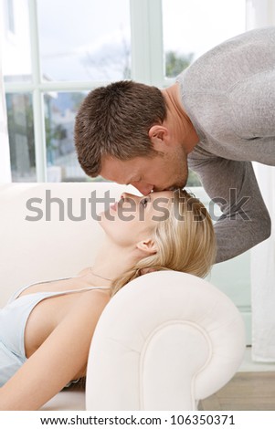Man kissing woman on the forehead while lounging at home.