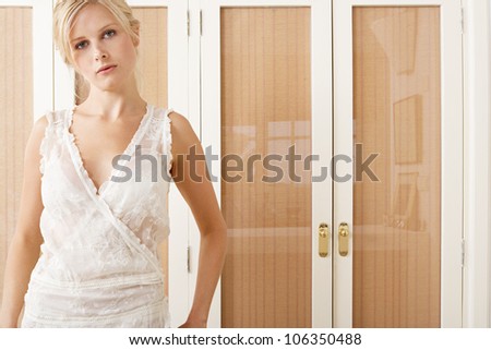 Attractive young woman standing in bedroom by wardrobe wearing a pretty night dress.