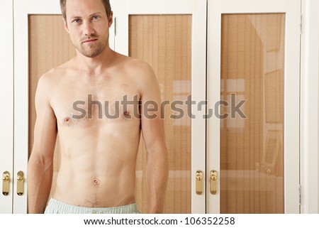 Attractive man in front of wardrobe doors in a bedroom in underwear, smiling.