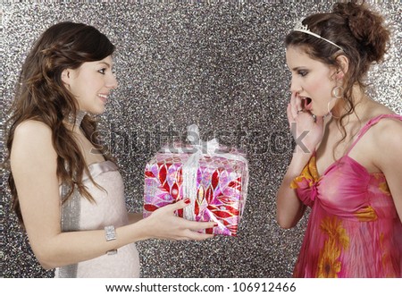 Girl giving a wrapped gift to her friend against a silver glitter background.