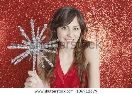 Attractive young woman holding a Christmas star against a red glitter background, smiling.
