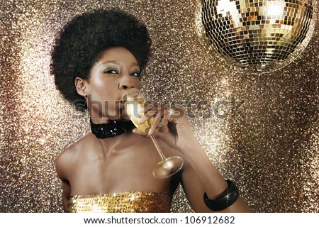Attractive black woman drinking champagne in a nightclub and drinking champagne next to a disco ball.