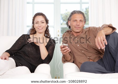 Mature couple sharing headphones while listening to music at home.