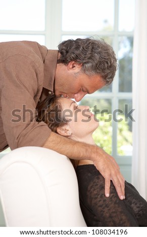 Mature man kissing woman\'s forehead while lounging at home\'s living room.