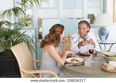 Mature couple eating and drinking together at garden table, while having a lively conversation.