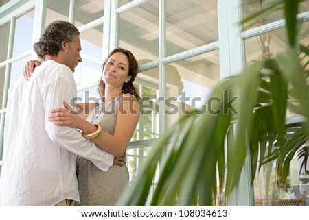 Mature couple hugging in a home terrace with large french doors.