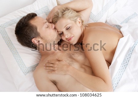 Young attractive man kissing woman's forehead in bed.