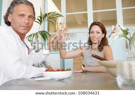 Mature couple toasting with champagne and eating strawberries, smiling.