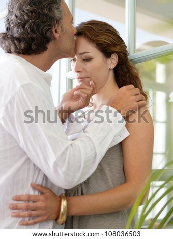 Close up of a mature couple kissing at home, standing by large glass doors.