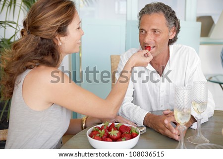 Woman feeding man strawberries while sitting on an outdoors table at home.