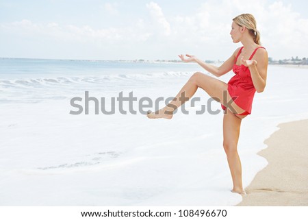 Attractive young woman balancing herself on one leg while practicing martial arts on the beach.