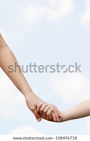 Close up of two young girls holding hands against the blue sky.