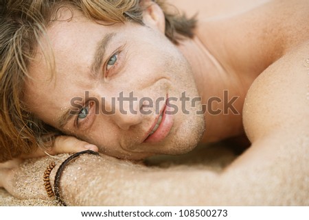 Close up portrait of an attractive young man sunbathing on the beach, smiling.