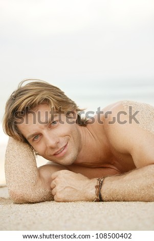Portrait of an attractive young man sunbathing on the beach, smiling.